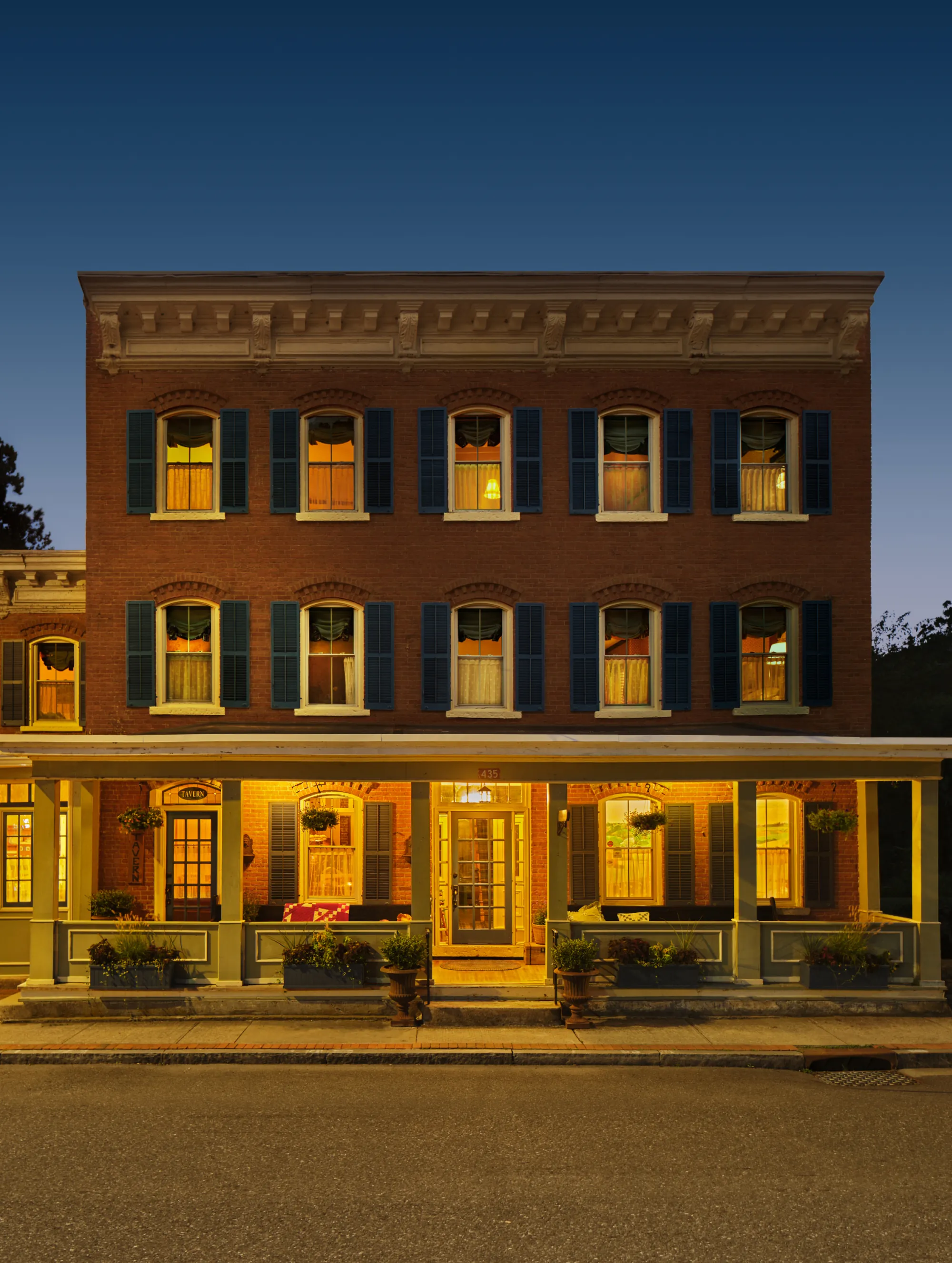 The Six Bells Countryside Inn at dusk, its 1850s brick facade and porch glowing with lamplight on Main Street in Rosendale.